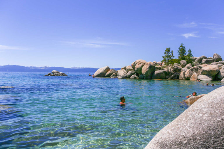 Swimmers in clear turquoise water near granite rocks at Chimney Beach in Lake Tahoe.