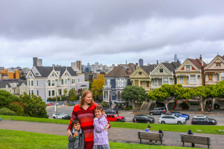 Family posing at Alamo Square Park with the Painted Ladies and San Francisco skyline in the background.
