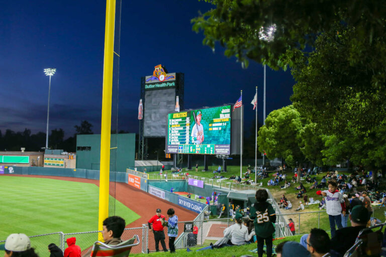 Families watching an Athletics game from the outfield grass berm at Sutter Health Park in Sacramento.